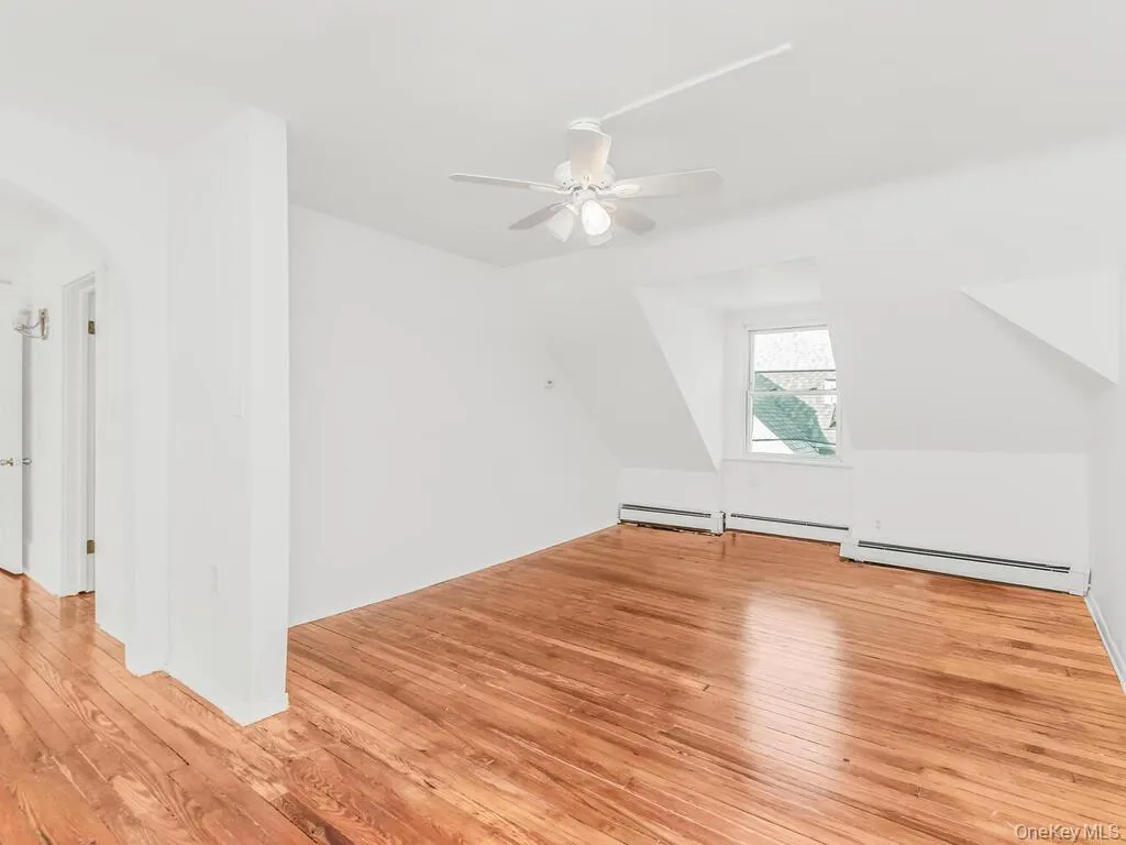 Additional living space featuring light wood-style floors, lofted ceiling, arched walkways, ceiling fan, and a baseboard heating unit Additional living space featuring light wood-style floors, lofted ceiling, arched walkways, ceiling fan, and a baseboard heating unit