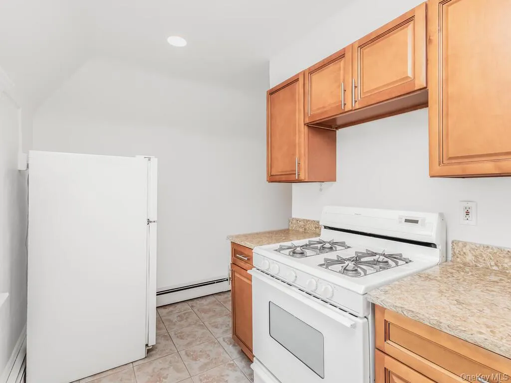 Kitchen featuring white appliances, light tile patterned floors, a baseboard heating unit, brown cabinetry, and recessed lighting Kitchen featuring white appliances, light tile patterned floors, a baseboard heating unit, brown cabinetry, and recessed lighting