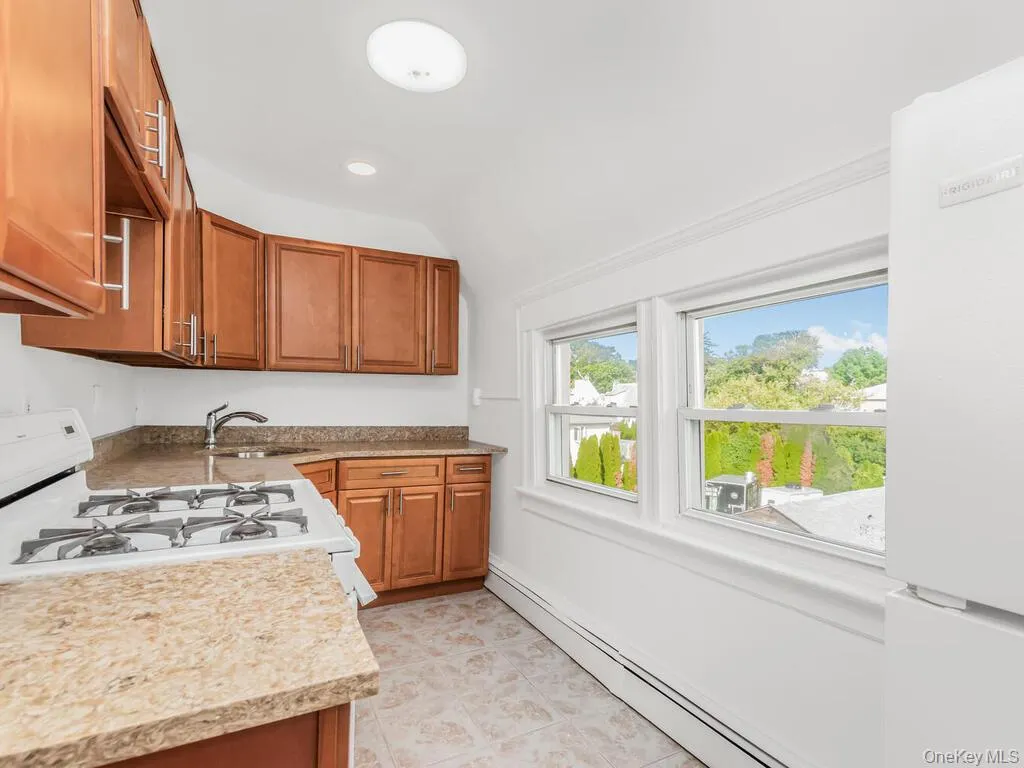 Kitchen featuring brown cabinetry, white appliances, a baseboard radiator, light countertops, and recessed lighting Kitchen featuring brown cabinetry, white appliances, a baseboard radiator, light countertops, and recessed lighting