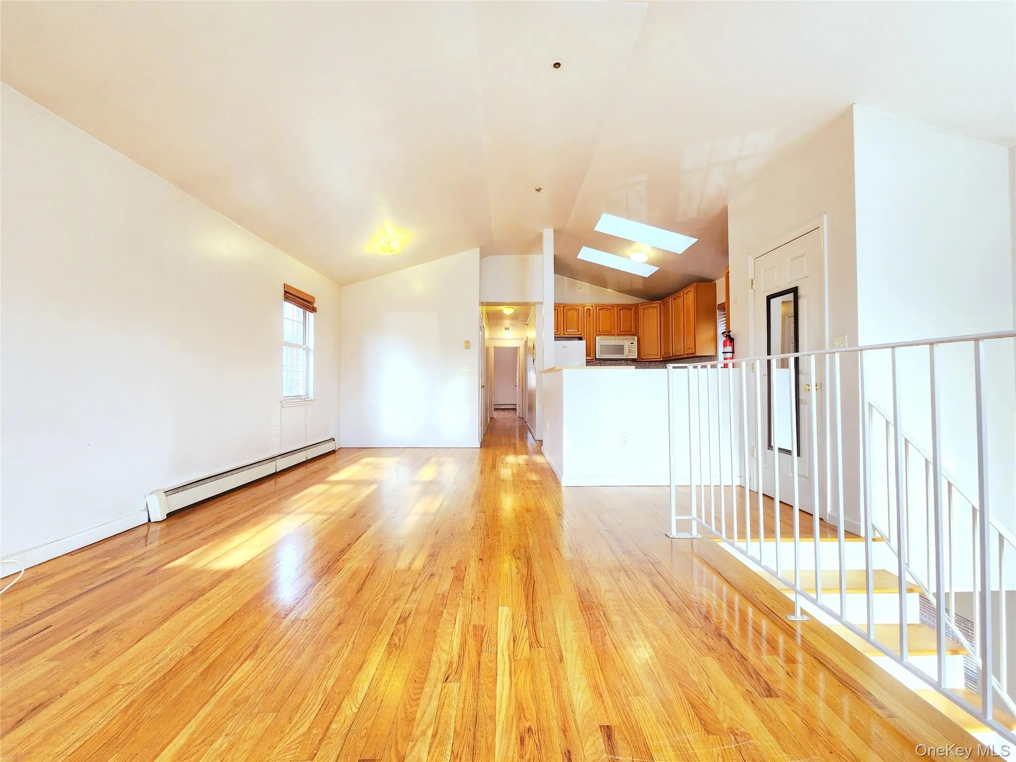 Unfurnished living room featuring vaulted ceiling, a skylight, light wood-type flooring, and a baseboard heating unit Unfurnished living room featuring vaulted ceiling, a skylight, light wood-type flooring, and a baseboard heating unit