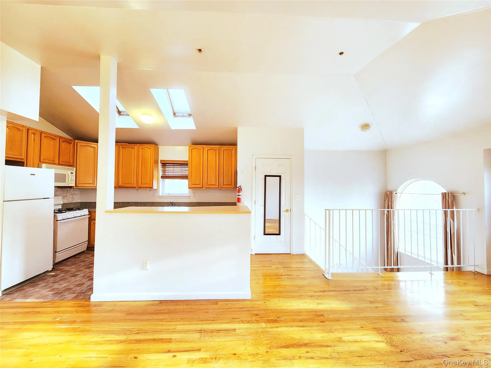 Kitchen featuring white appliances, a skylight, lofted ceiling, light wood-style floors, and brown cabinetry Kitchen featuring white appliances, a skylight, lofted ceiling, light wood-style floors, and brown cabinetry
