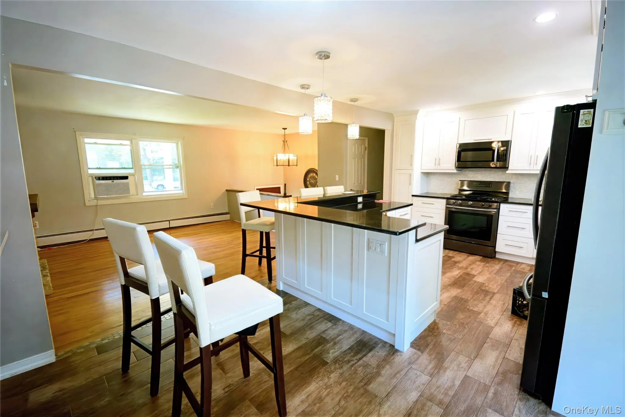 Kitchen featuring appliances with stainless steel finishes, a breakfast bar area, white cabinetry, decorative backsplash, and decorative light fixtures Kitchen featuring appliances with stainless steel finishes, a breakfast bar area, white cabinetry, decorative backsplash, and decorative light fixtures