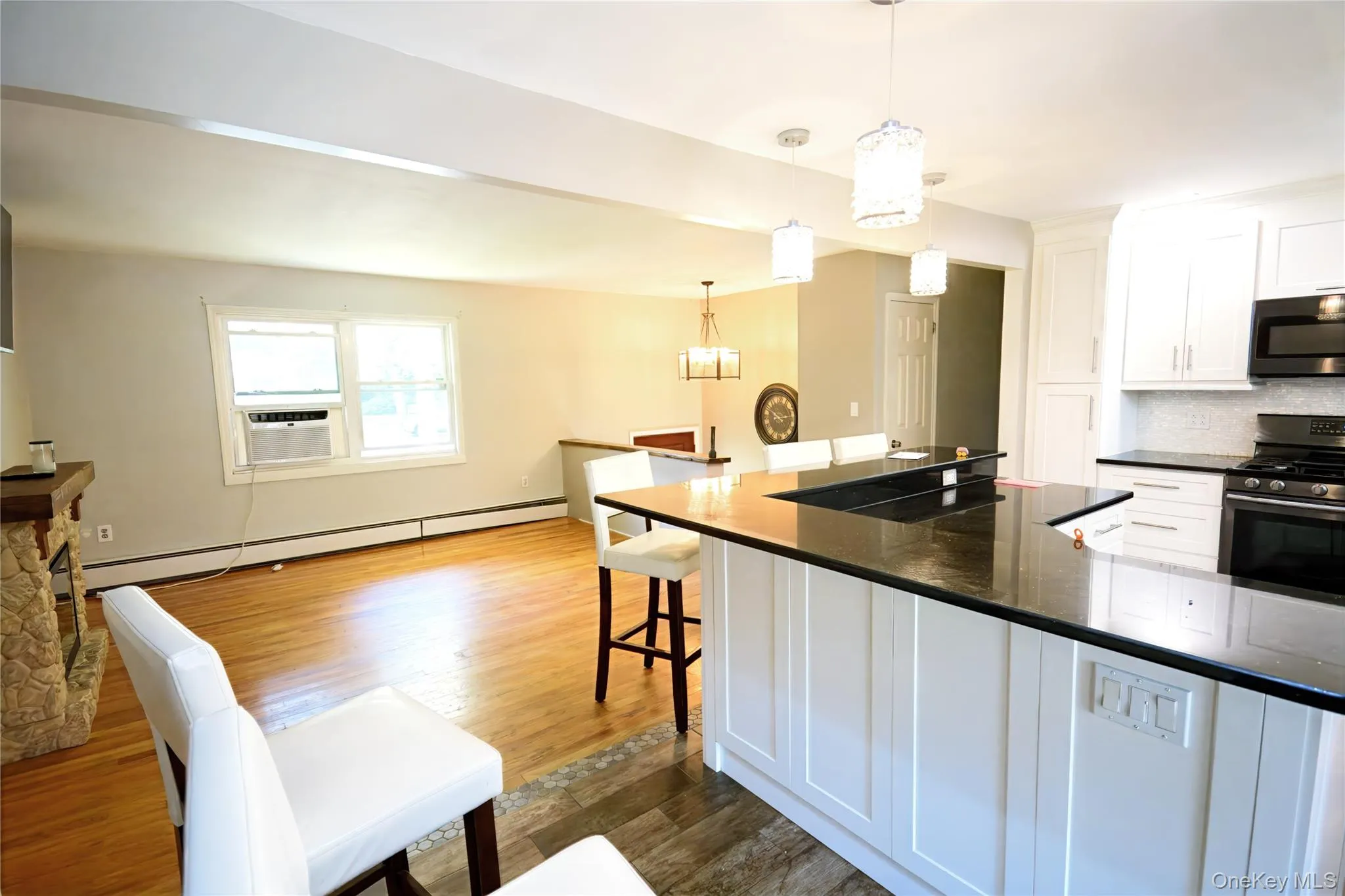 Kitchen featuring appliances with stainless steel finishes, a breakfast bar area, white cabinets, a baseboard heating unit, and hanging light fixtures Kitchen featuring appliances with stainless steel finishes, a breakfast bar area, white cabinets, a baseboard heating unit, and hanging light fixtures