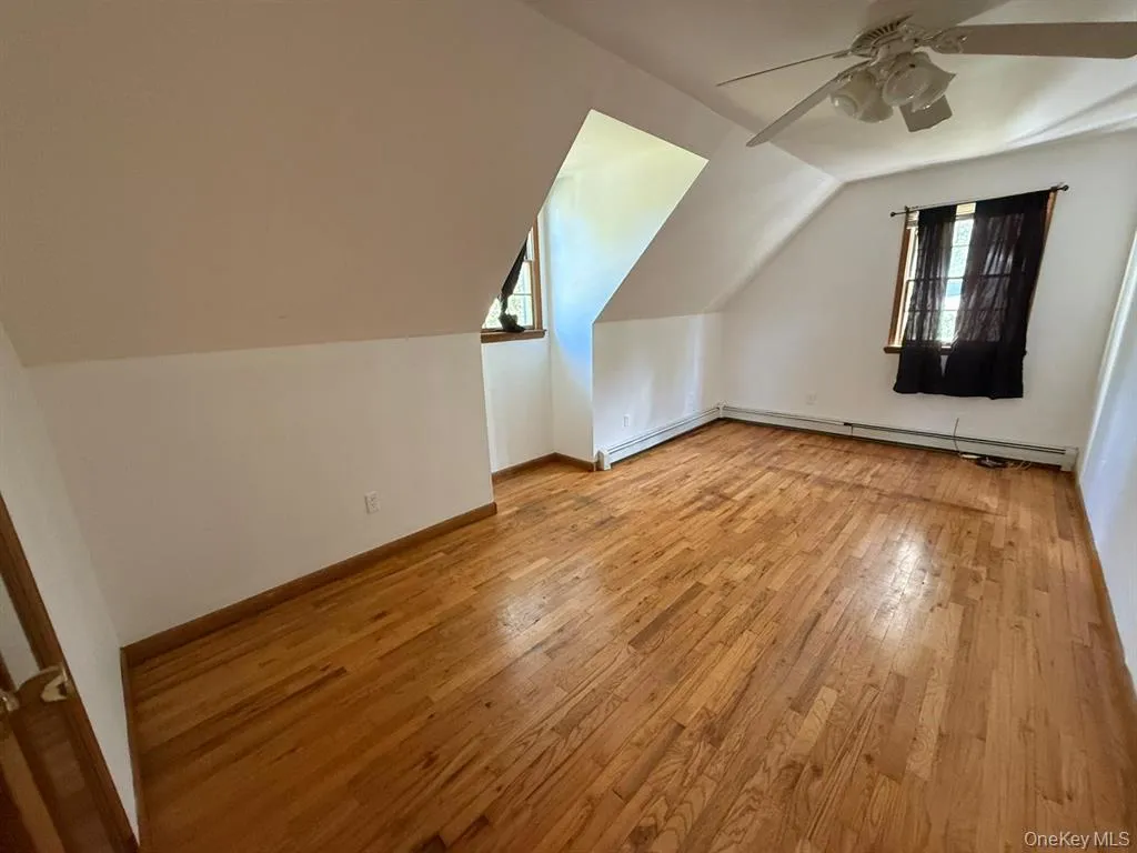 Additional living space with light wood finished floors, lofted ceiling, baseboard heating, and a ceiling fan Additional living space with light wood finished floors, lofted ceiling, baseboard heating, and a ceiling fan