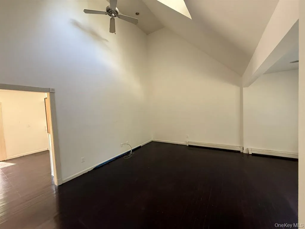 Additional living space with high vaulted ceiling, a ceiling fan, dark wood-type flooring, and baseboard heating Additional living space with high vaulted ceiling, a ceiling fan, dark wood-type flooring, and baseboard heating