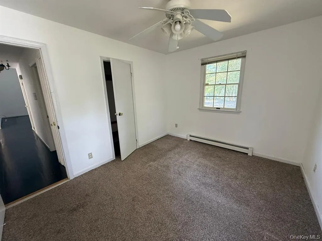 Unfurnished bedroom with a baseboard heating unit, dark colored carpet, and ceiling fan Unfurnished bedroom with a baseboard heating unit, dark colored carpet, and ceiling fan