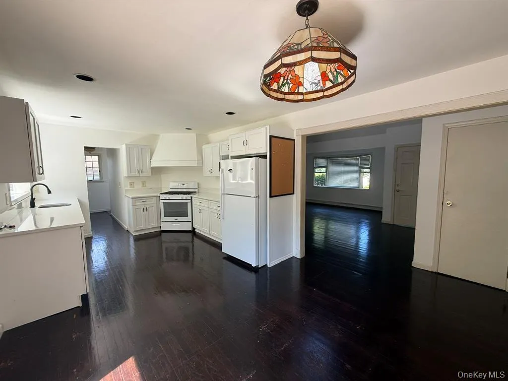 Kitchen with white appliances, white cabinets, dark wood-style flooring, and healthy amount of natural light Kitchen with white appliances, white cabinets, dark wood-style flooring, and healthy amount of natural light