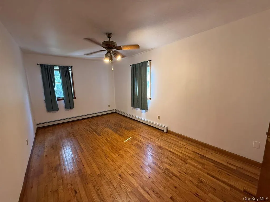 Empty room featuring light wood-style flooring, a baseboard radiator, and a ceiling fan Empty room featuring light wood-style flooring, a baseboard radiator, and a ceiling fan