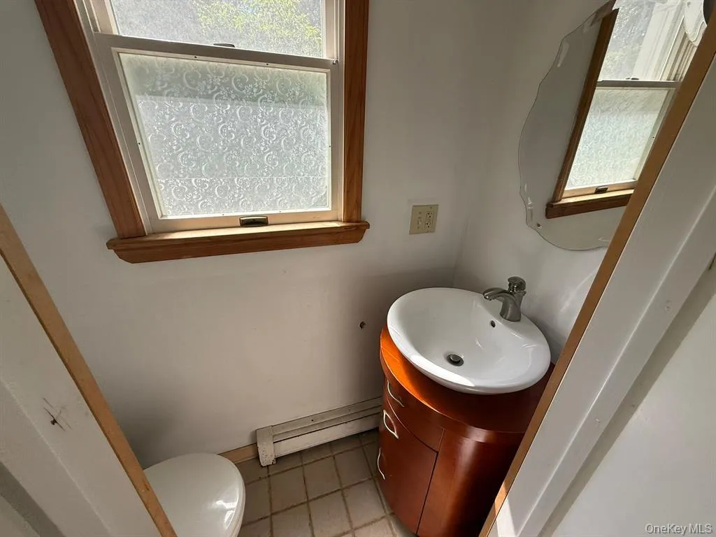 Bathroom featuring vanity, light tile patterned floors, a baseboard radiator, and plenty of natural light Bathroom featuring vanity, light tile patterned floors, a baseboard radiator, and plenty of natural light