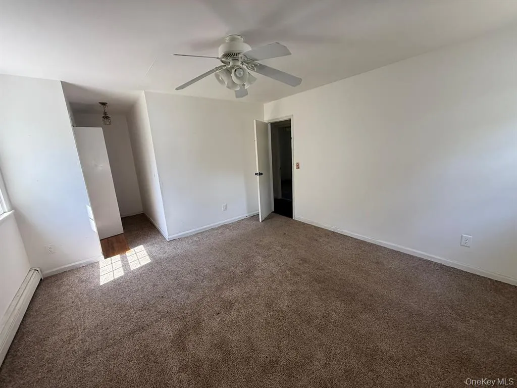 Unfurnished bedroom featuring a baseboard heating unit, carpet, ceiling fan, and a walk in closet Unfurnished bedroom featuring a baseboard heating unit, carpet, ceiling fan, and a walk in closet