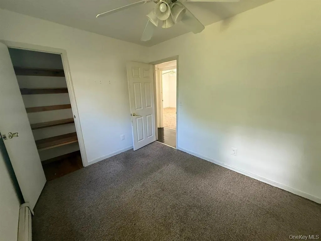 Unfurnished bedroom with a spacious closet, dark colored carpet, and ceiling fan Unfurnished bedroom with a spacious closet, dark colored carpet, and ceiling fan