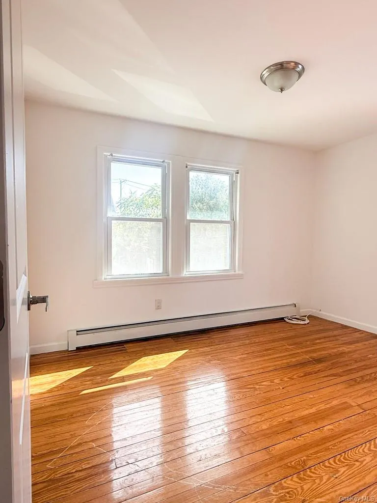 Unfurnished room with light wood finished floors and baseboard heating Unfurnished room with light wood finished floors and baseboard heating