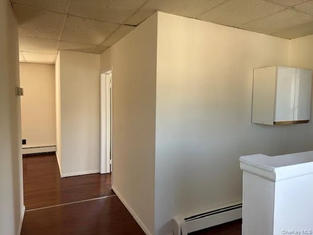 Hall featuring baseboard heating, a drop ceiling, and dark wood finished floors Hall featuring baseboard heating, a drop ceiling, and dark wood finished floors