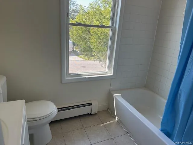 Bathroom featuring baseboard heating, light tile patterned floors, shower / tub combo with curtain, and vanity Bathroom featuring baseboard heating, light tile patterned floors, shower / tub combo with curtain, and vanity