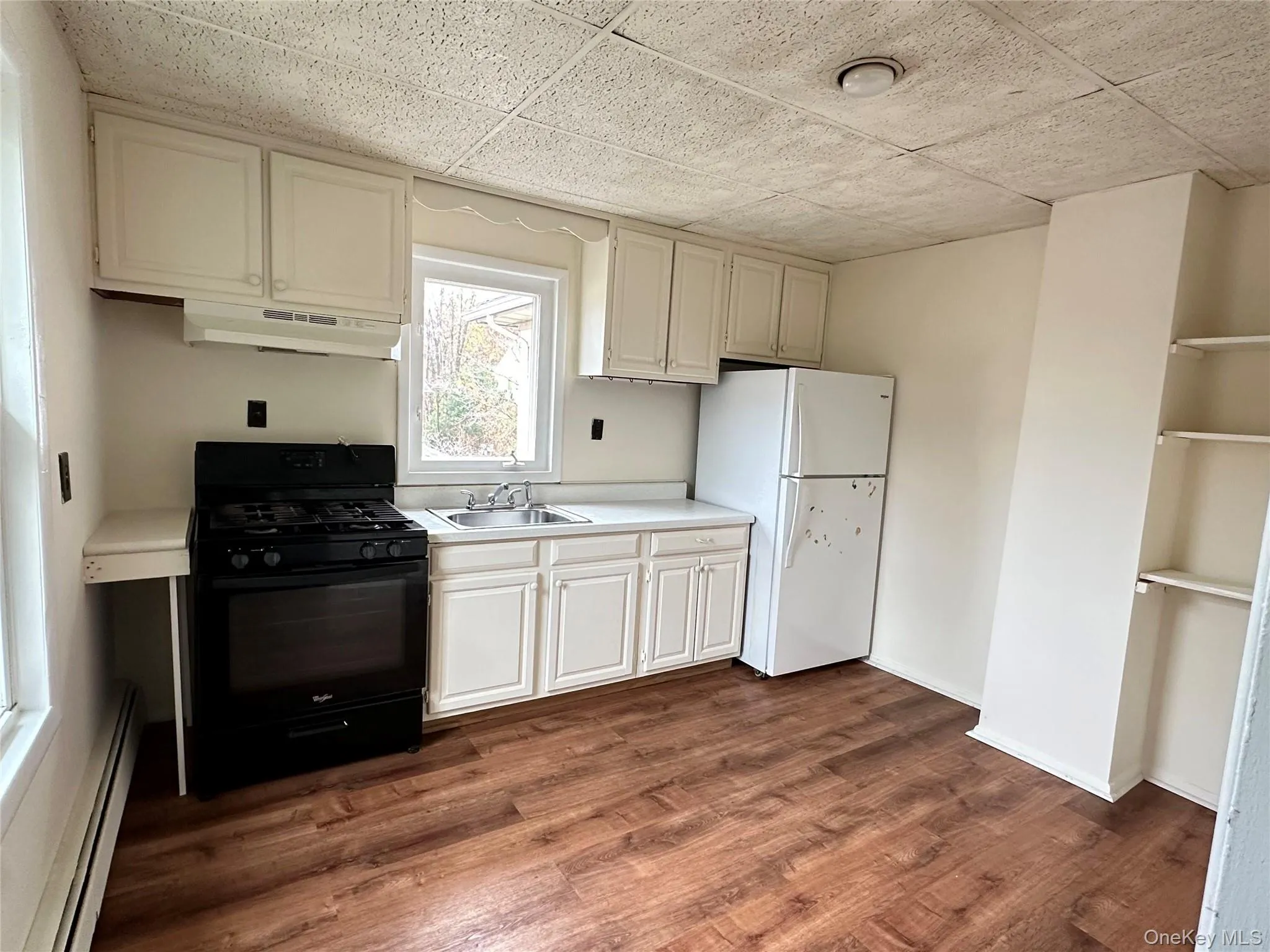 Kitchen featuring black range with gas cooktop, a baseboard heating unit, freestanding refrigerator, light countertops, and under cabinet range hood Kitchen featuring black range with gas cooktop, a baseboard heating unit, freestanding refrigerator, light countertops, and under cabinet range hood