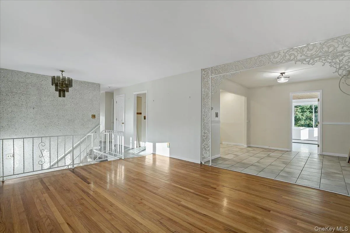 Unfurnished living room featuring wood finished floors, arched walkways, a chandelier, and baseboard heating Unfurnished living room featuring wood finished floors, arched walkways, a chandelier, and baseboard heating