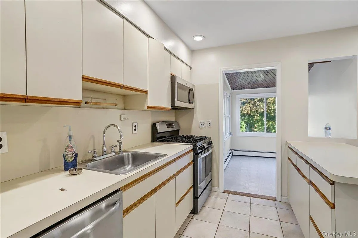Kitchen featuring white cabinetry, stainless steel appliances, light countertops, light tile patterned flooring, and brown cabinetry Kitchen featuring white cabinetry, stainless steel appliances, light countertops, light tile patterned flooring, and brown cabinetry