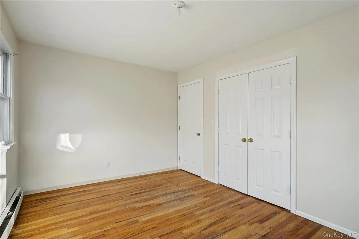 Unfurnished bedroom featuring baseboard heating, light wood-style floors, a closet, and multiple windows Unfurnished bedroom featuring baseboard heating, light wood-style floors, a closet, and multiple windows