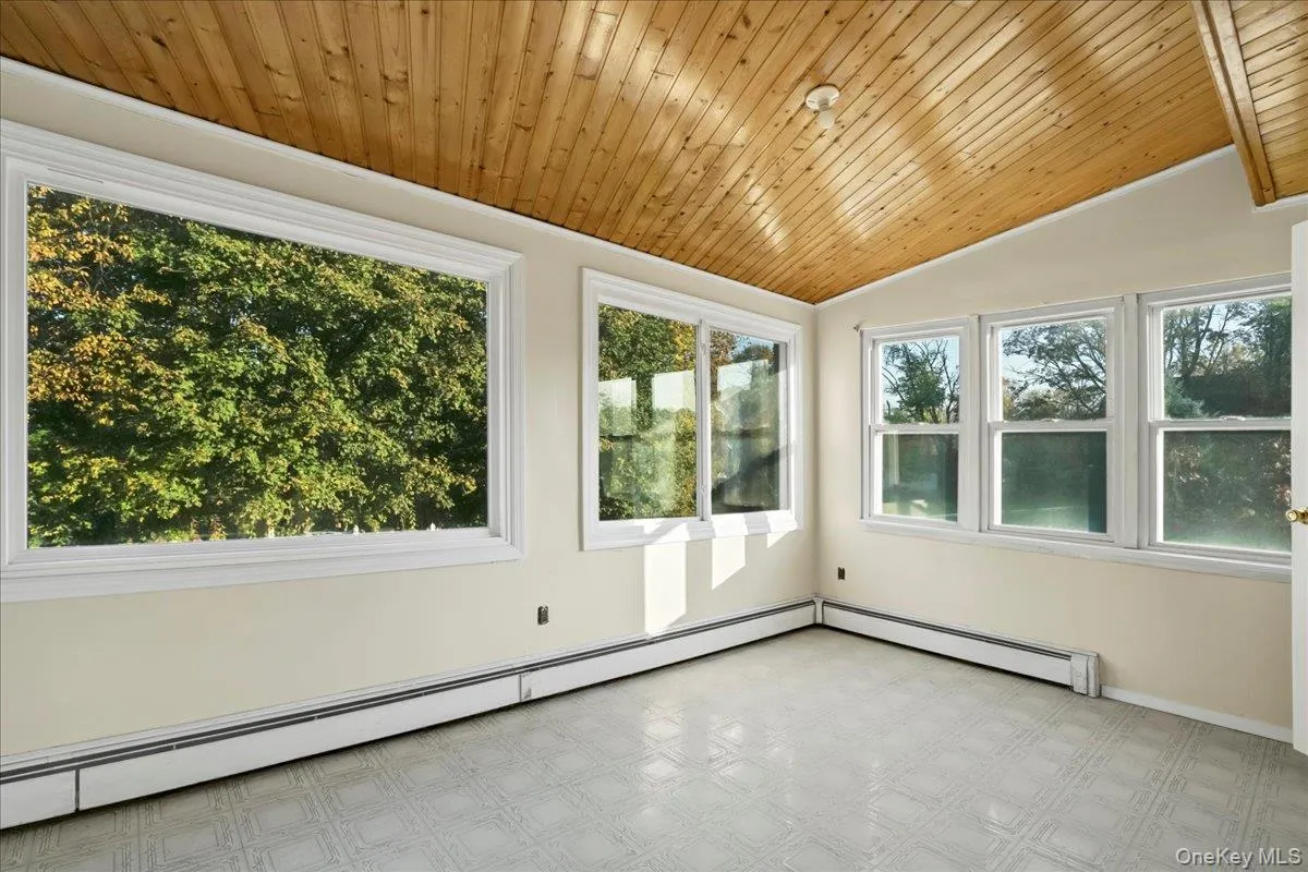Unfurnished sunroom featuring lofted ceiling, baseboard heating, and plenty of natural light Unfurnished sunroom featuring lofted ceiling, baseboard heating, and plenty of natural light
