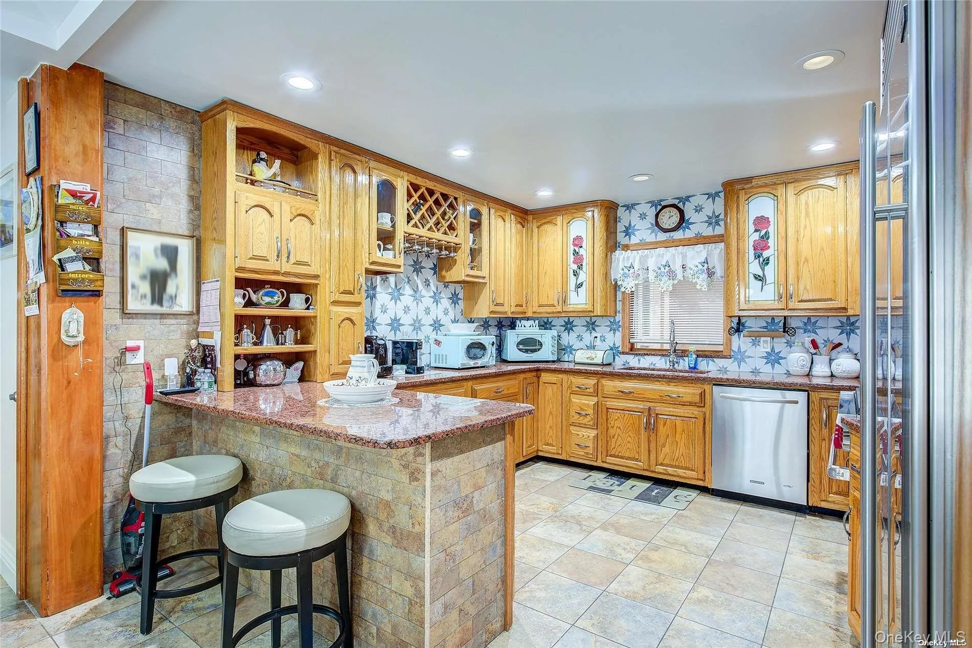 Kitchen featuring a breakfast bar, stainless steel appliances, light stone countertops, glass insert cabinets, and a peninsula Kitchen featuring a breakfast bar, stainless steel appliances, light stone countertops, glass insert cabinets, and a peninsula