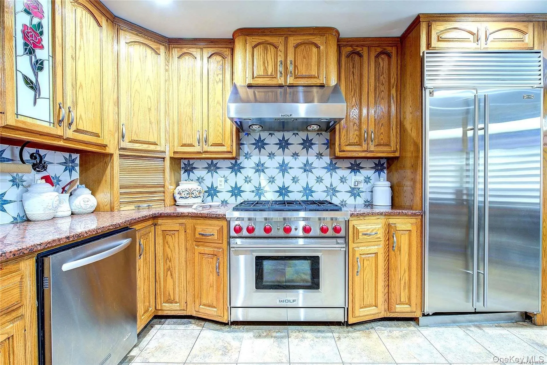 Kitchen featuring high quality appliances, light stone counters, under cabinet range hood, and decorative backsplash Kitchen featuring high quality appliances, light stone counters, under cabinet range hood, and decorative backsplash