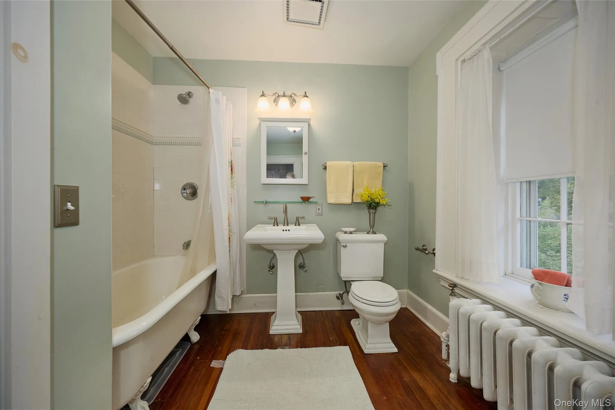 Bathroom featuring radiator, dark wood-style flooring, and shower / bath combo with shower curtain Bathroom featuring radiator, dark wood-style flooring, and shower / bath combo with shower curtain