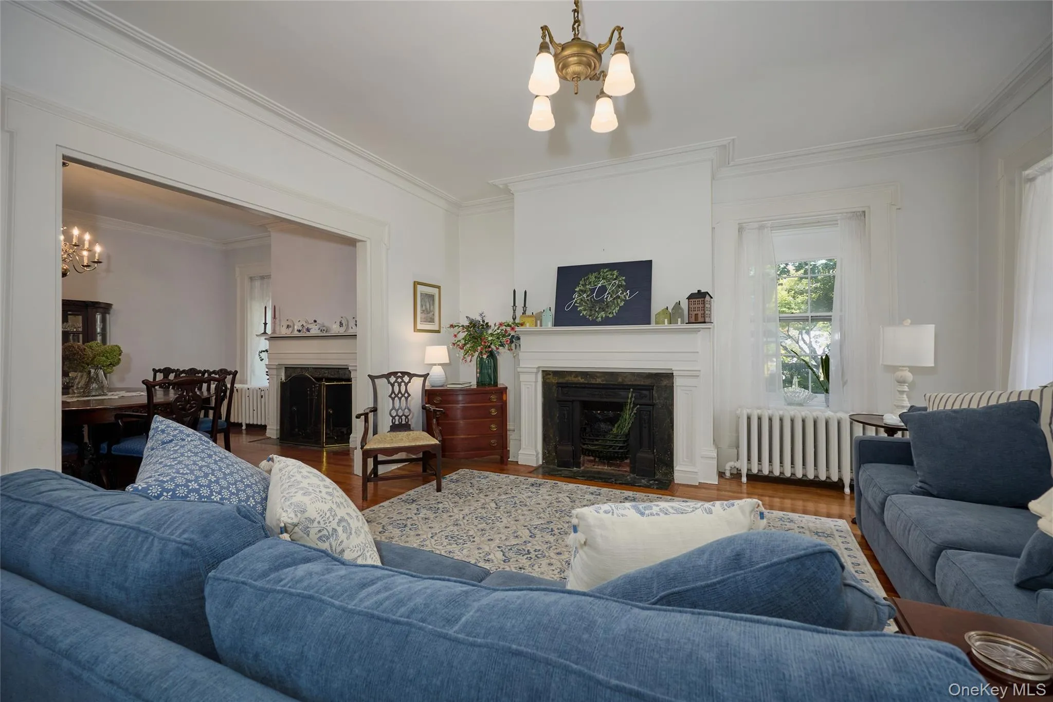 Living area featuring a fireplace with flush hearth, a chandelier, radiator heating unit, crown molding, and wood finished floors Living area featuring a fireplace with flush hearth, a chandelier, radiator heating unit, crown molding, and wood finished floors