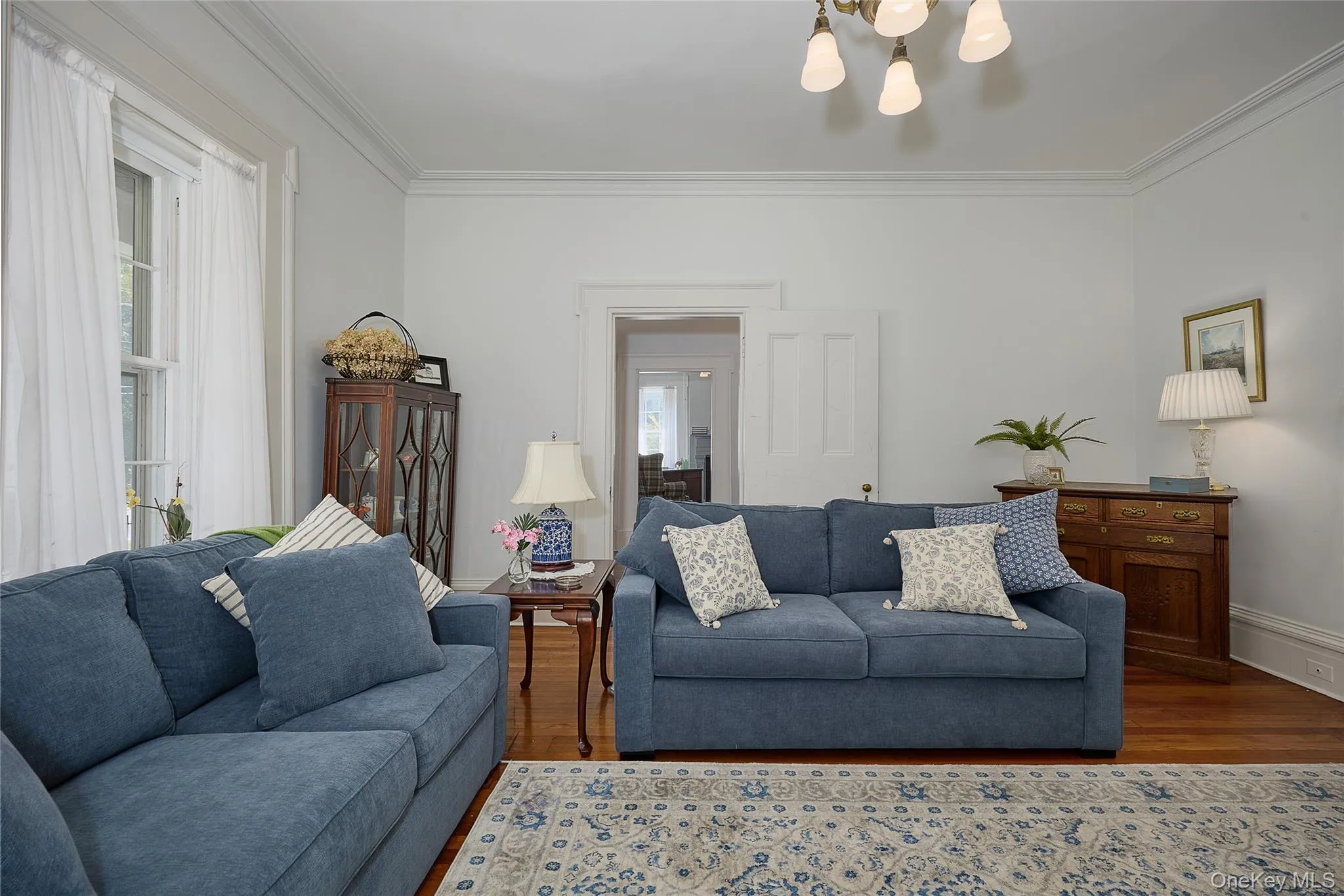 Living room with wood finished floors, ornamental molding, and a chandelier Living room with wood finished floors, ornamental molding, and a chandelier