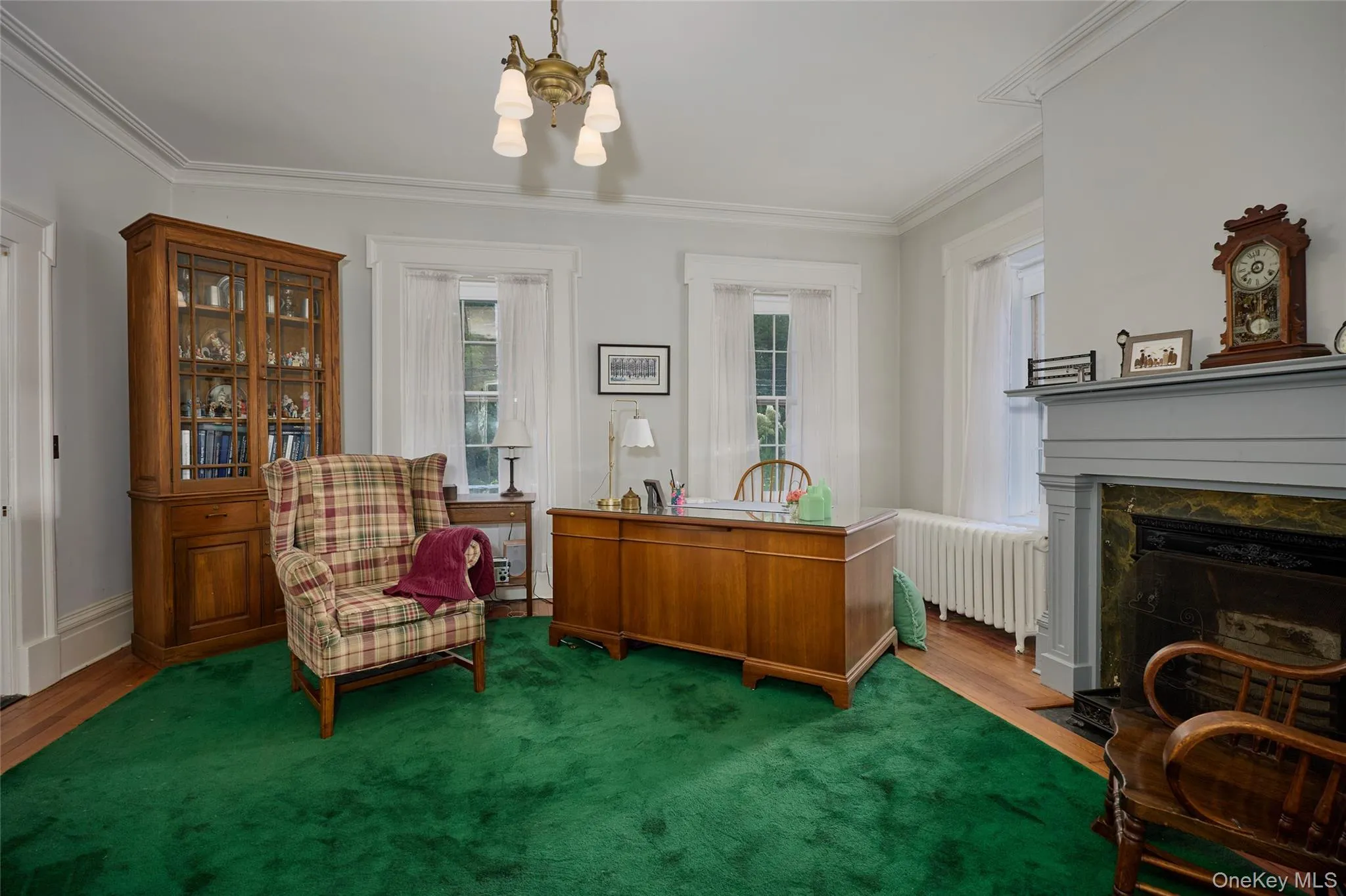 Living area featuring a chandelier, radiator heating unit, ornamental molding, a fireplace with flush hearth, and dark wood-style flooring Living area featuring a chandelier, radiator heating unit, ornamental molding, a fireplace with flush hearth, and dark wood-style flooring