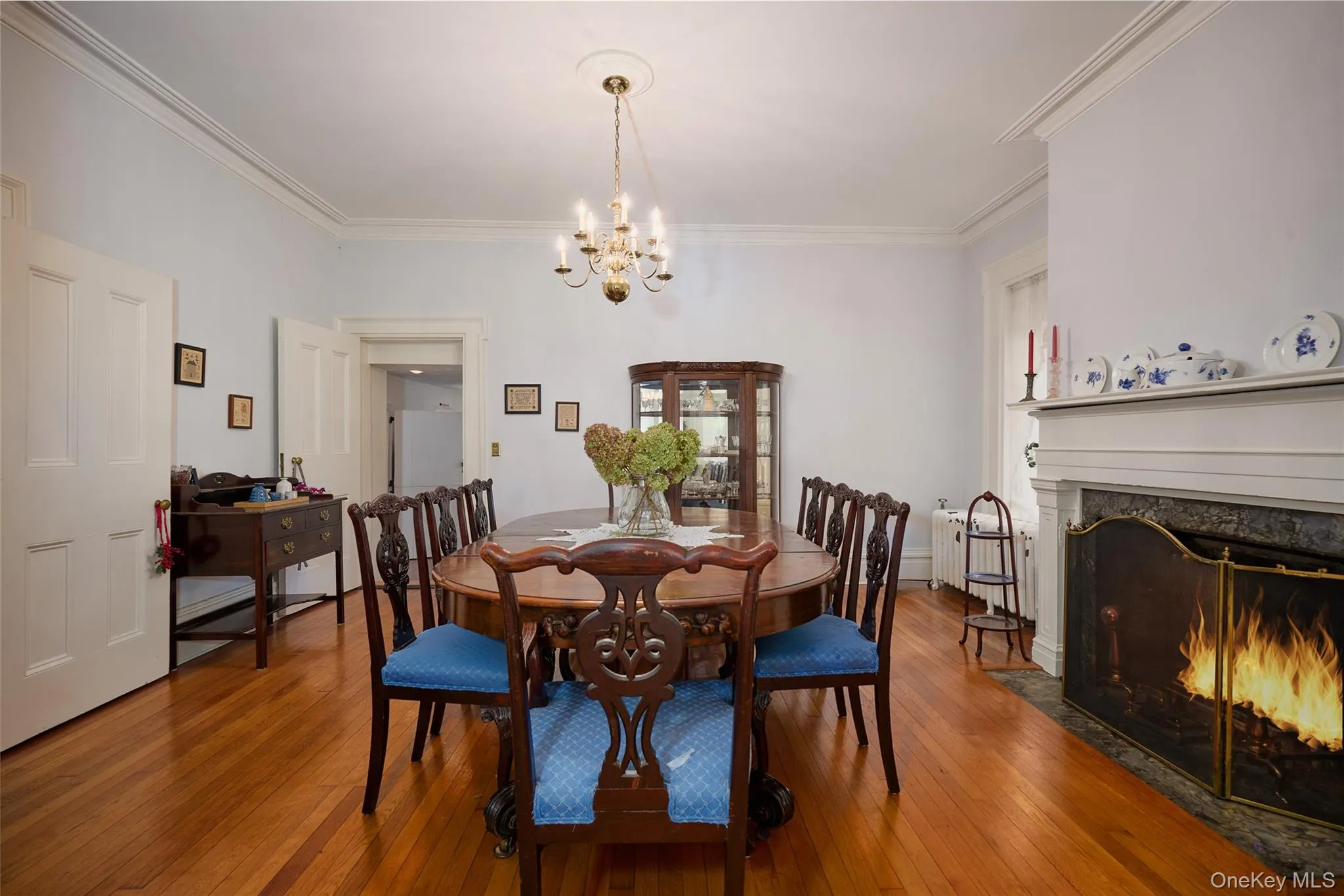 Dining space featuring crown molding, hardwood / wood-style flooring, a premium fireplace, a chandelier, and radiator Dining space featuring crown molding, hardwood / wood-style flooring, a premium fireplace, a chandelier, and radiator