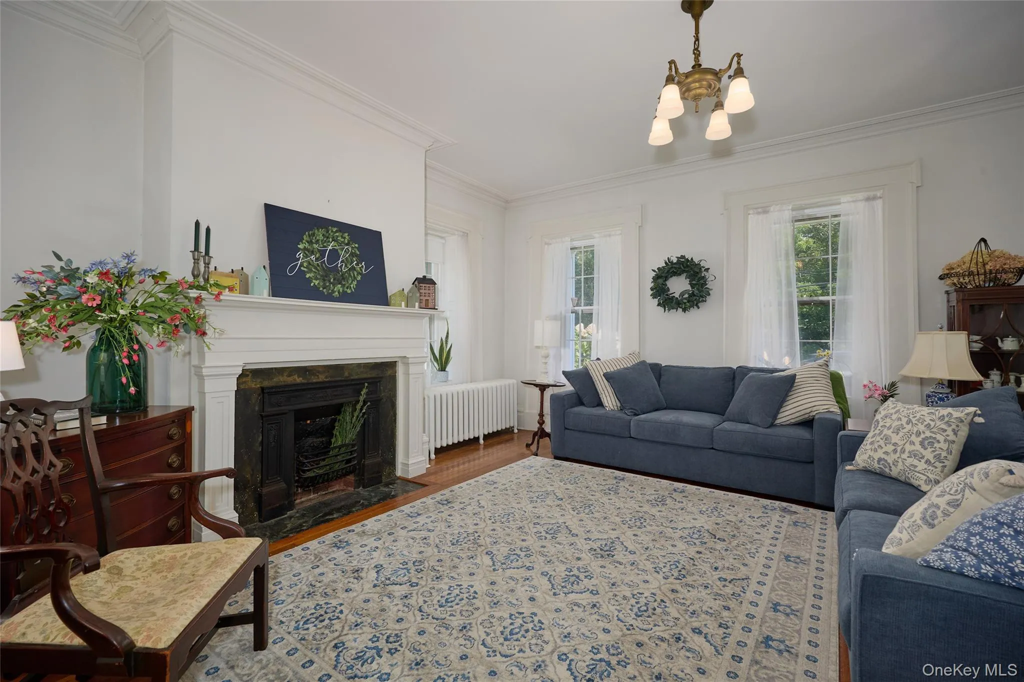 Living room featuring crown molding, radiator, wood finished floors, a chandelier, and a premium fireplace Living room featuring crown molding, radiator, wood finished floors, a chandelier, and a premium fireplace