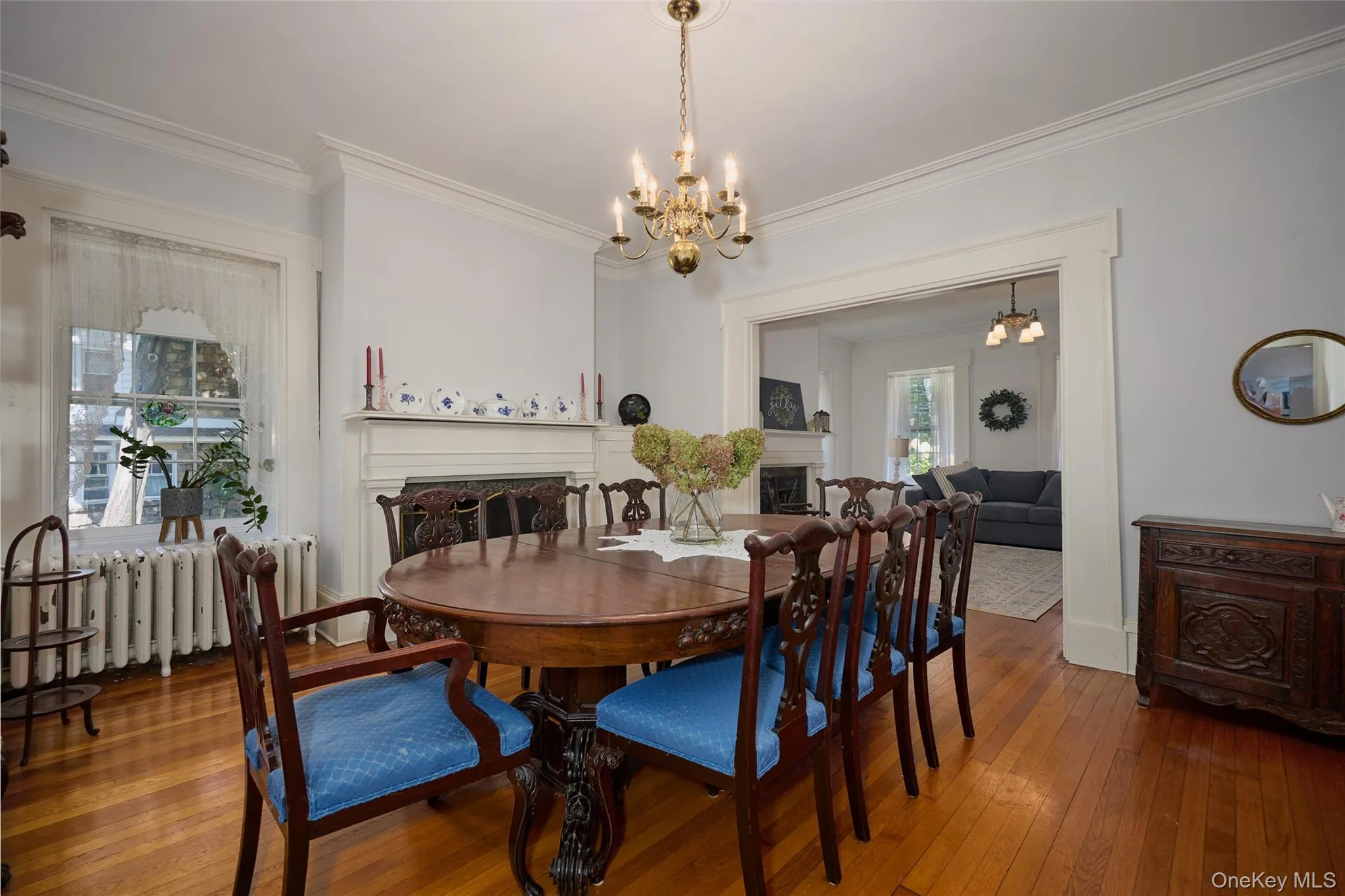 Dining room featuring a fireplace, a chandelier, wood-type flooring, ornamental molding, and radiator heating unit Dining room featuring a fireplace, a chandelier, wood-type flooring, ornamental molding, and radiator heating unit