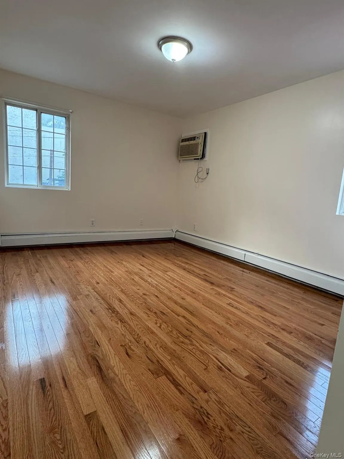 Unfurnished room with light wood-style floors, a baseboard radiator, and an AC wall unit Unfurnished room with light wood-style floors, a baseboard radiator, and an AC wall unit