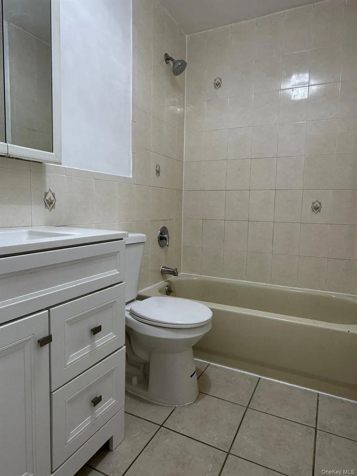 Bathroom featuring washtub / shower combination, vanity, light tile patterned floors, and tile walls Bathroom featuring washtub / shower combination, vanity, light tile patterned floors, and tile walls