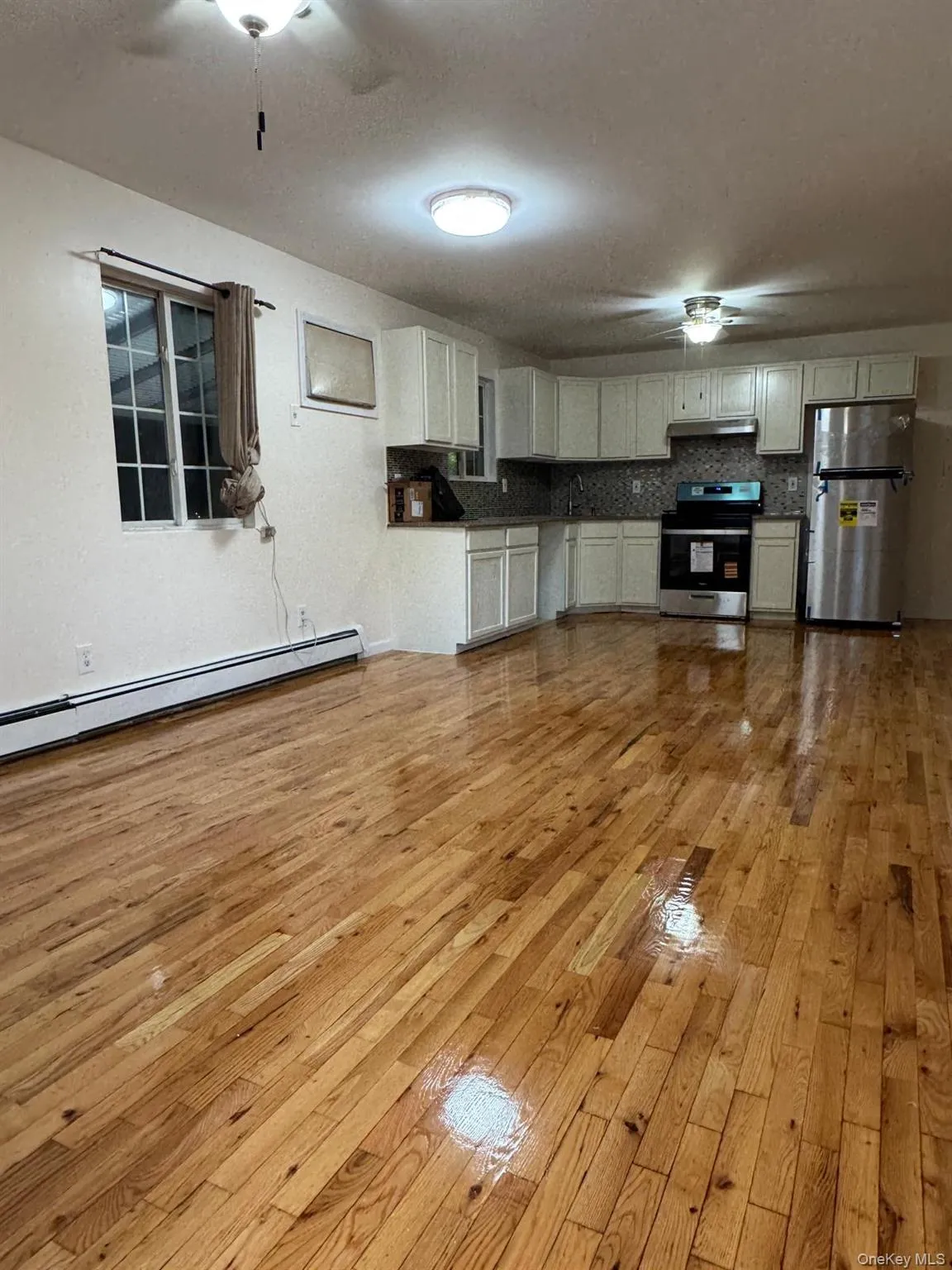 Kitchen featuring a ceiling fan, dark countertops, a baseboard heating unit, light wood-style floors, and stainless steel appliances Kitchen featuring a ceiling fan, dark countertops, a baseboard heating unit, light wood-style floors, and stainless steel appliances