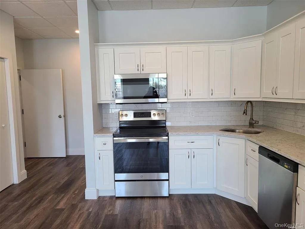 Kitchen with stainless steel appliances, white cabinets, backsplash, and a paneled ceiling Kitchen with stainless steel appliances, white cabinets, backsplash, and a paneled ceiling