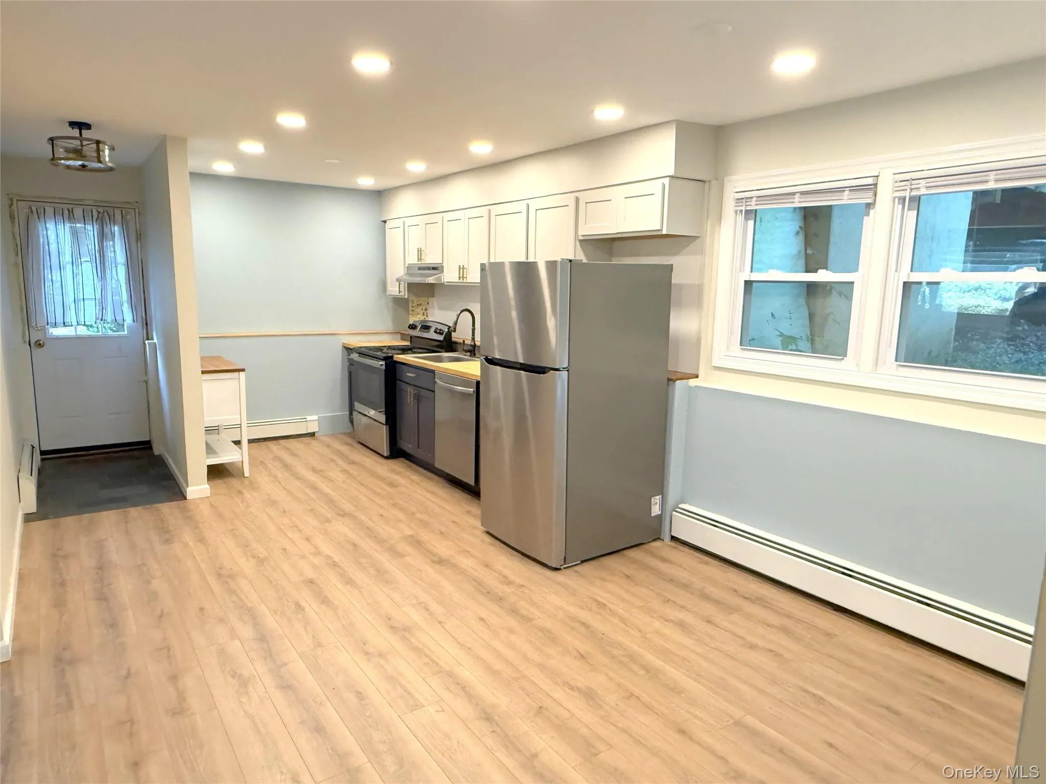 Kitchen with white cabinets, appliances with stainless steel finishes, a baseboard heating unit, light wood-style floors, and recessed lighting Kitchen with white cabinets, appliances with stainless steel finishes, a baseboard heating unit, light wood-style floors, and recessed lighting