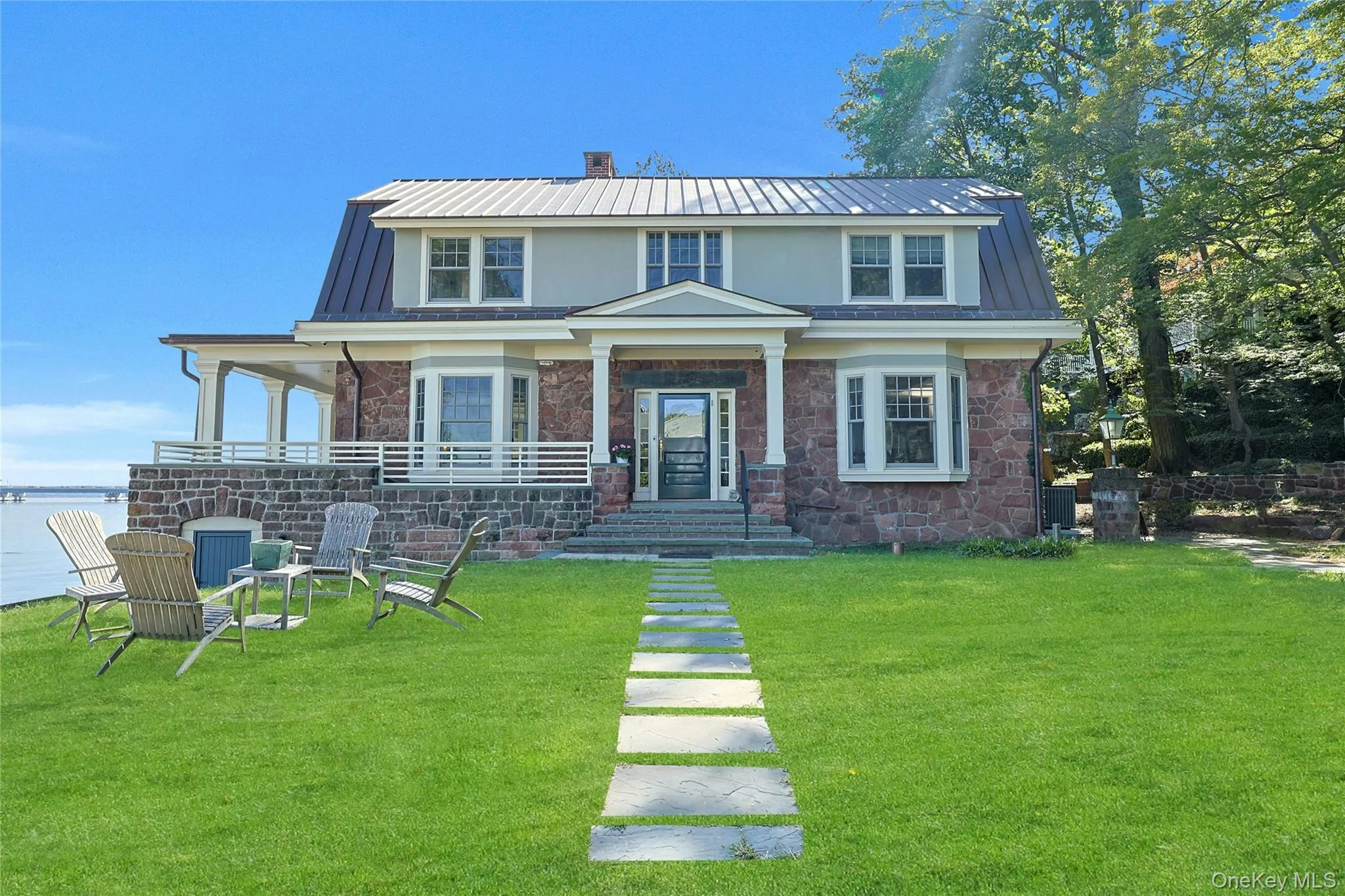 View of front of home featuring a metal roof, a chimney, stone siding, and a front lawn View of front of home featuring a metal roof, a chimney, stone siding, and a front lawn