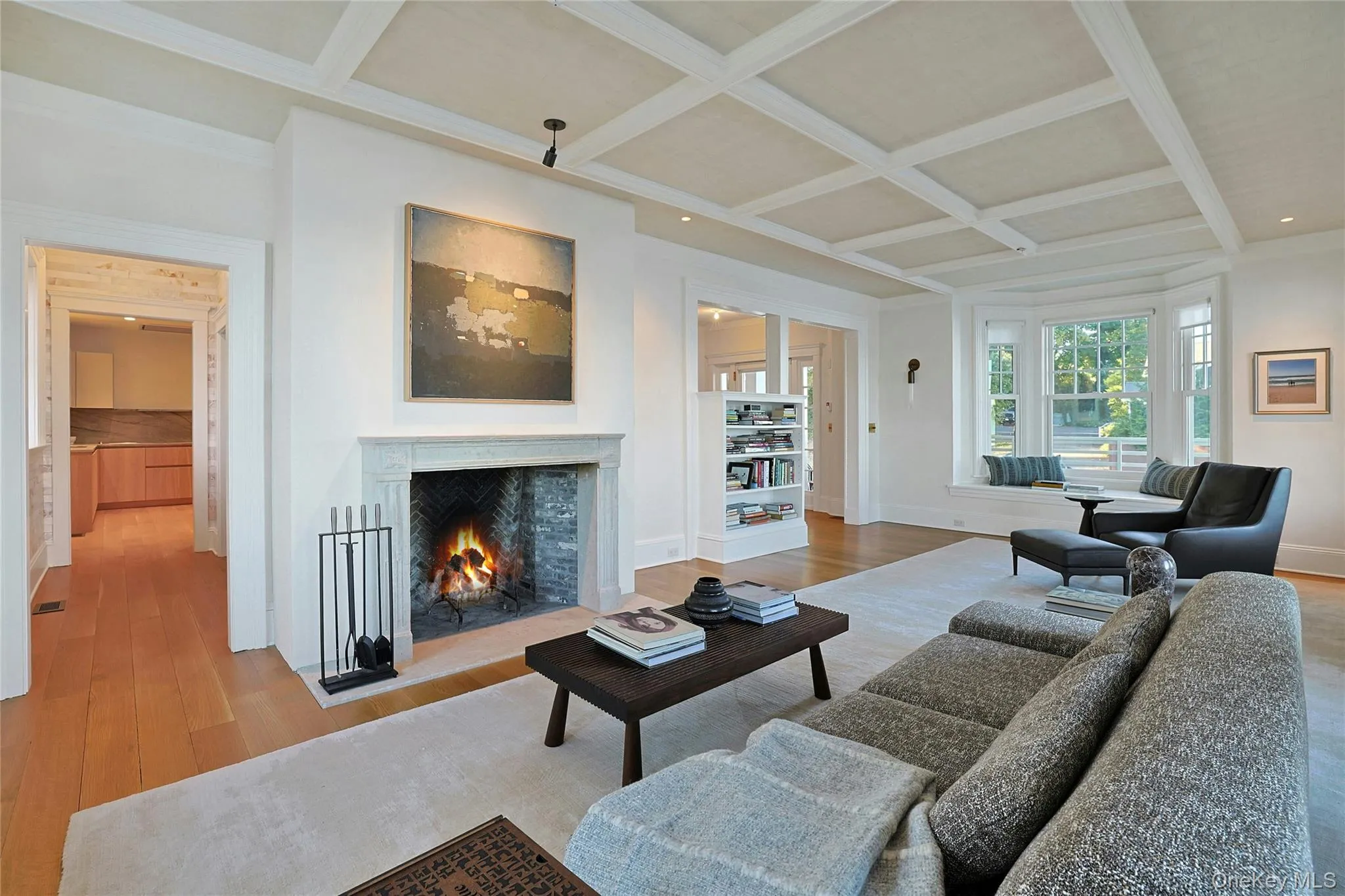Living room with coffered ceiling, a warm lit fireplace, beam ceiling, and wood finished floors Living room with coffered ceiling, a warm lit fireplace, beam ceiling, and wood finished floors
