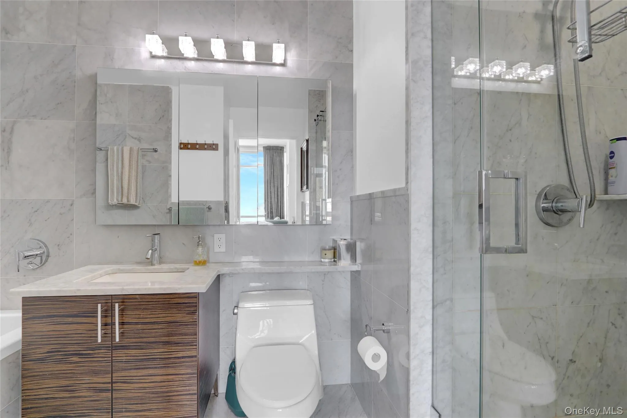 Bathroom featuring tile walls, vanity, and a marble finish shower Bathroom featuring tile walls, vanity, and a marble finish shower
