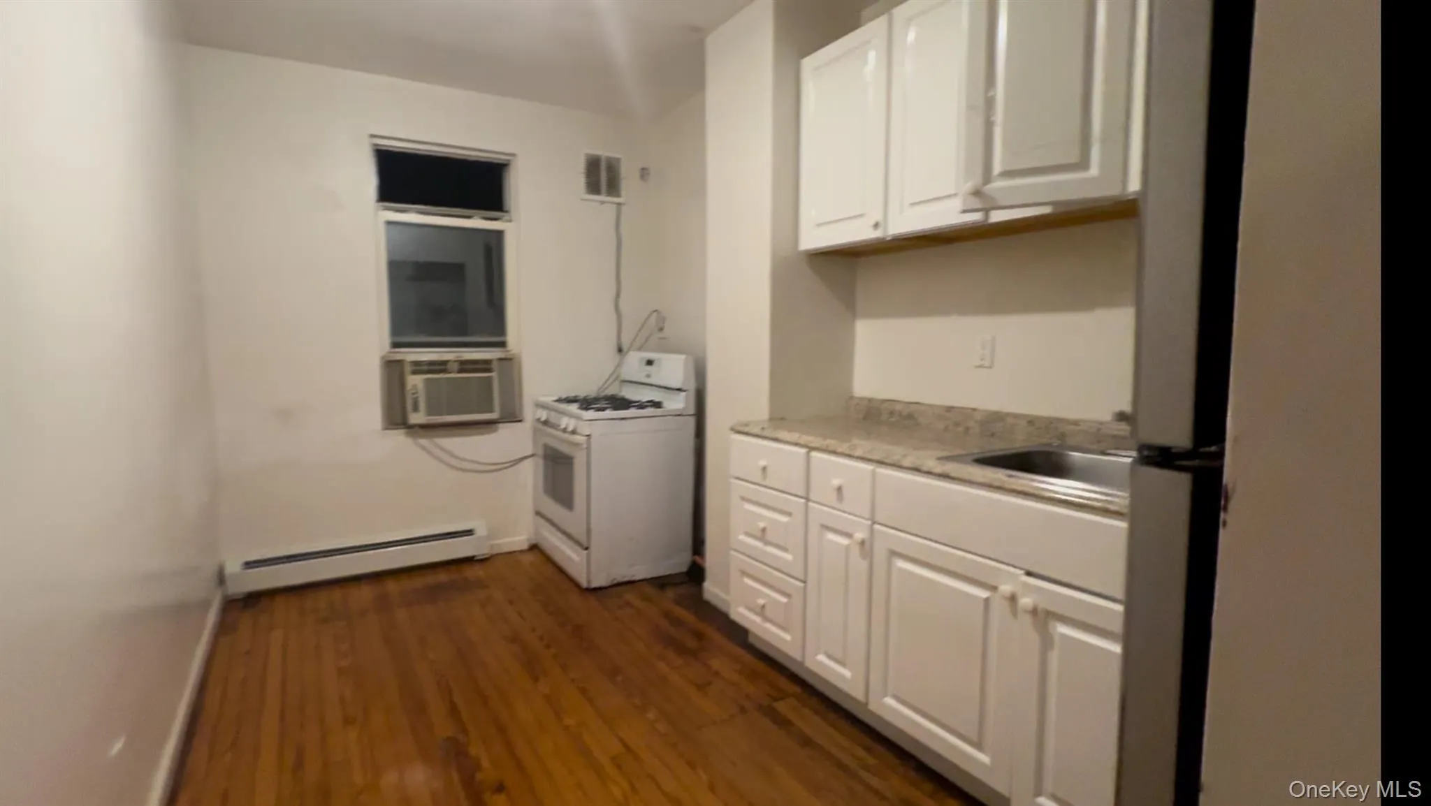 Kitchen featuring white cabinets, white range with gas stovetop, dark wood-style flooring, baseboard heating, and cooling unit Kitchen featuring white cabinets, white range with gas stovetop, dark wood-style flooring, baseboard heating, and cooling unit