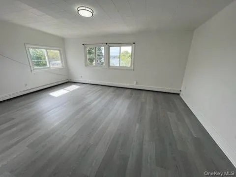 Spare room with wood finished floors, healthy amount of natural light, and a baseboard heating unit Spare room with wood finished floors, healthy amount of natural light, and a baseboard heating unit