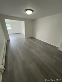 Unfurnished living room with dark wood-style floors and a baseboard heating unit Unfurnished living room with dark wood-style floors and a baseboard heating unit