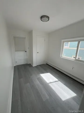 Unfurnished bedroom with a baseboard radiator and wood finished floors Unfurnished bedroom with a baseboard radiator and wood finished floors
