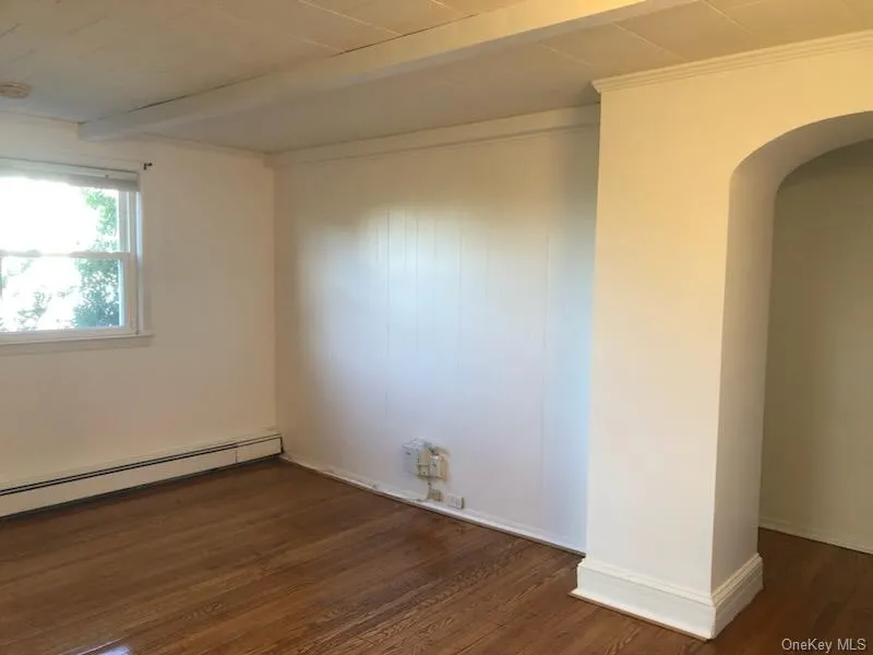 Empty room with beam ceiling, dark wood finished floors, and arched walkways Empty room with beam ceiling, dark wood finished floors, and arched walkways