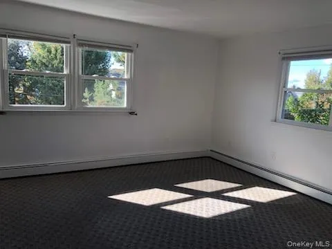 Unfurnished room featuring dark colored carpet, baseboard heating, and a baseboard heating unit Unfurnished room featuring dark colored carpet, baseboard heating, and a baseboard heating unit