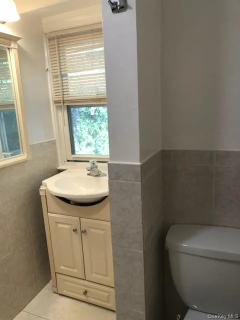 Bathroom with tile walls, vanity, light tile patterned floors, and a wainscoted wall Bathroom with tile walls, vanity, light tile patterned floors, and a wainscoted wall