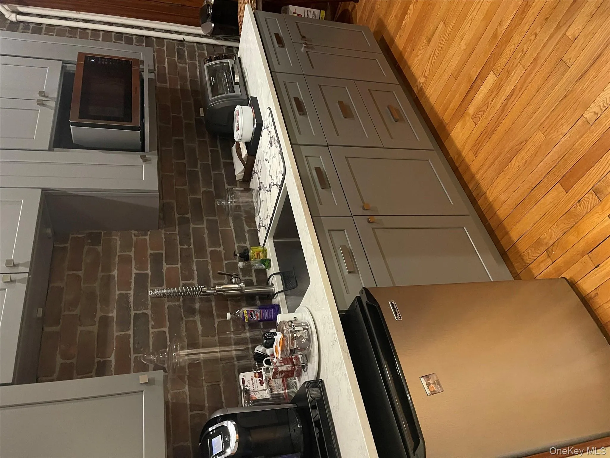 Kitchen featuring gray cabinetry, dishwashing machine, light wood-type flooring, decorative backsplash, and light stone counters Kitchen featuring gray cabinetry, dishwashing machine, light wood-type flooring, decorative backsplash, and light stone counters