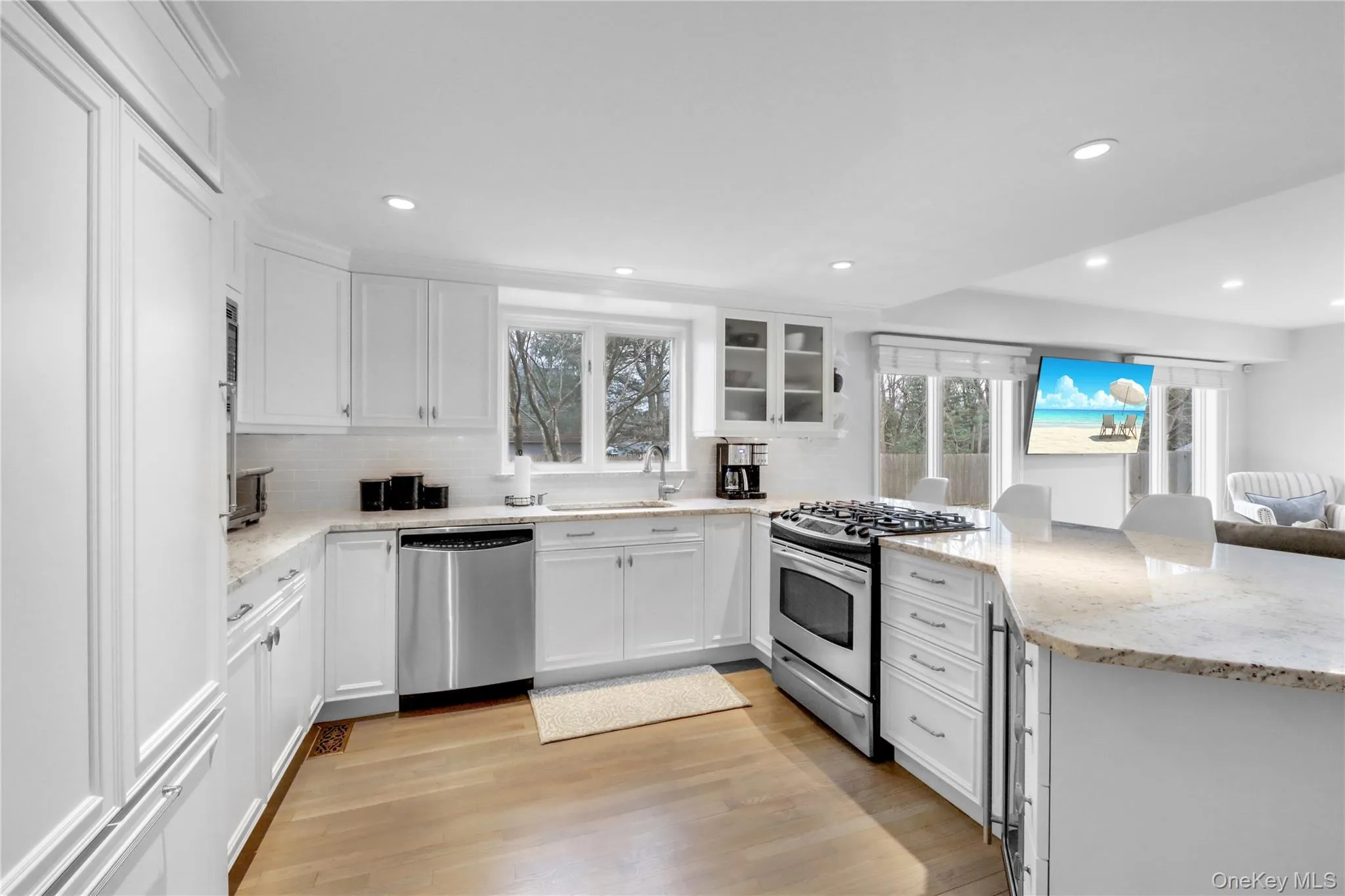 Kitchen with appliances with stainless steel finishes, white cabinetry, light stone countertops, backsplash, and glass insert cabinets Kitchen with appliances with stainless steel finishes, white cabinetry, light stone countertops, backsplash, and glass insert cabinets