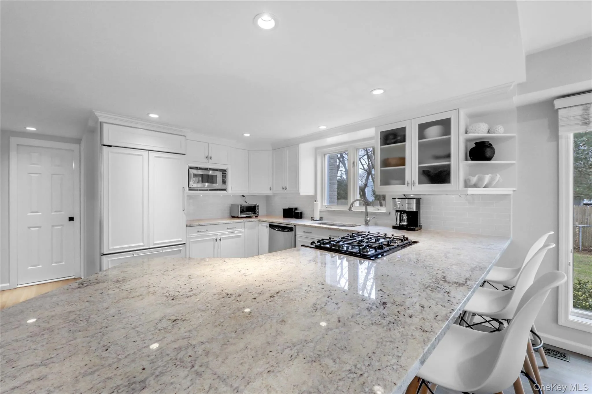 Kitchen featuring glass insert cabinets, a peninsula, a breakfast bar area, light stone countertops, and recessed lighting Kitchen featuring glass insert cabinets, a peninsula, a breakfast bar area, light stone countertops, and recessed lighting